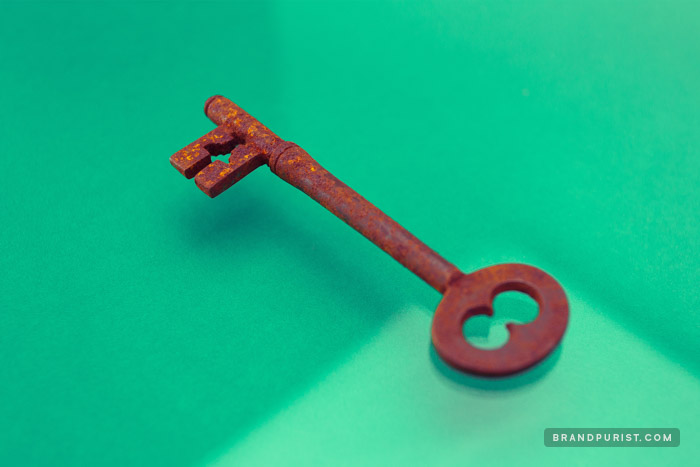 Rusted single antique key photographed against a vibrant green background.