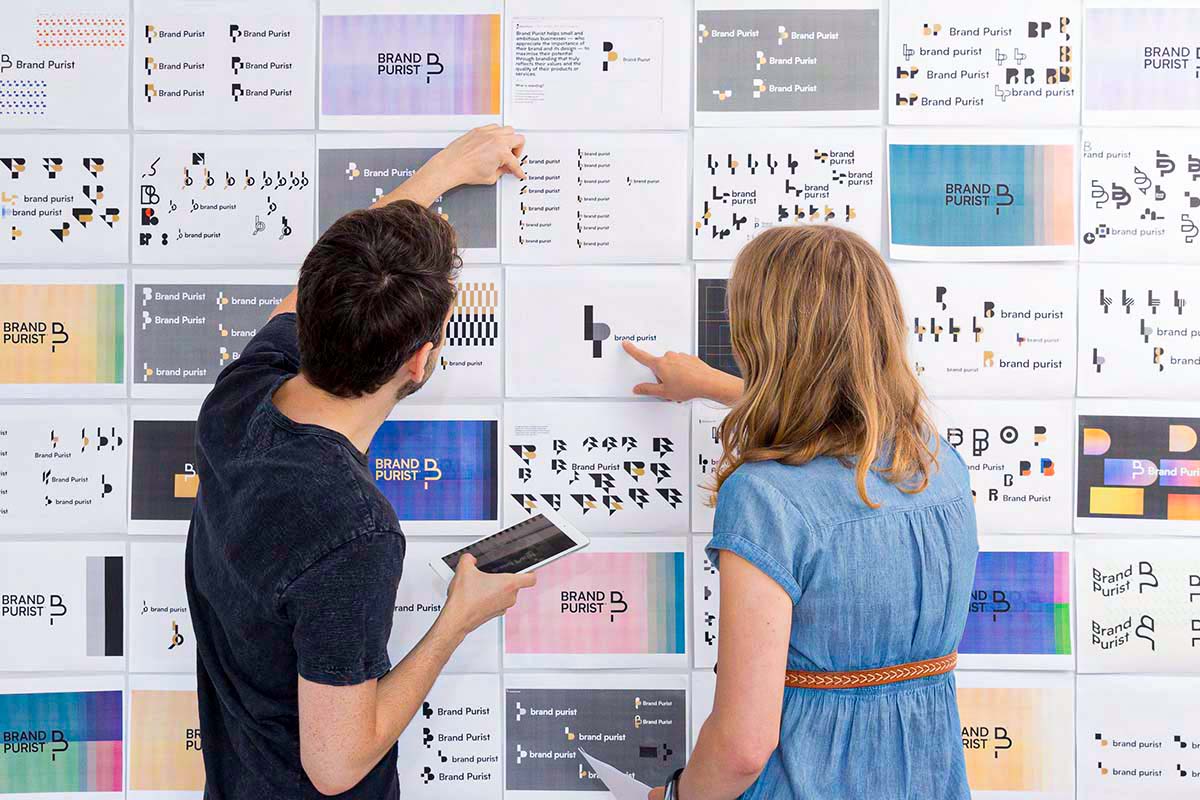 로고 개발 작업 프린트물로 덮인 벽을 보고 있는 디자이너들.