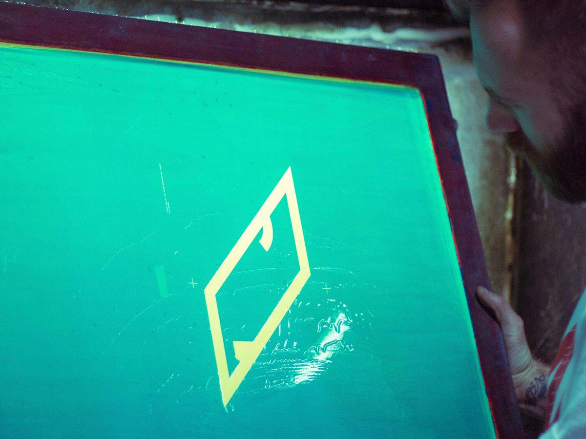 Ein Handwerker des ICON Printing Teams inspiziert ein Siebdruckgewebe mit dem diagonalen Symbol des Markenlogos in der Mitte.