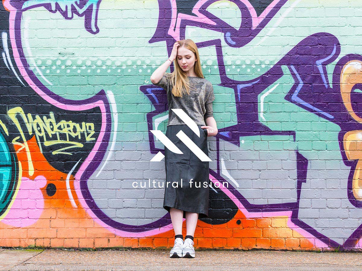 Lookbook-Foto eines Models vor einer Graffiti-Mauer mit dem Logo von URTA und dem Slogan ‚Cultural Fusion' darunter.