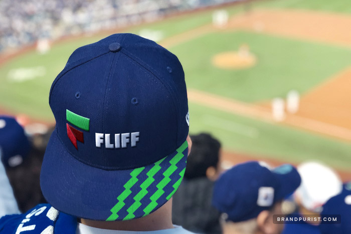 Man wearing a dark blue baseball cap with Fliff logo and green money pattern, overlooking a baseball stadium.