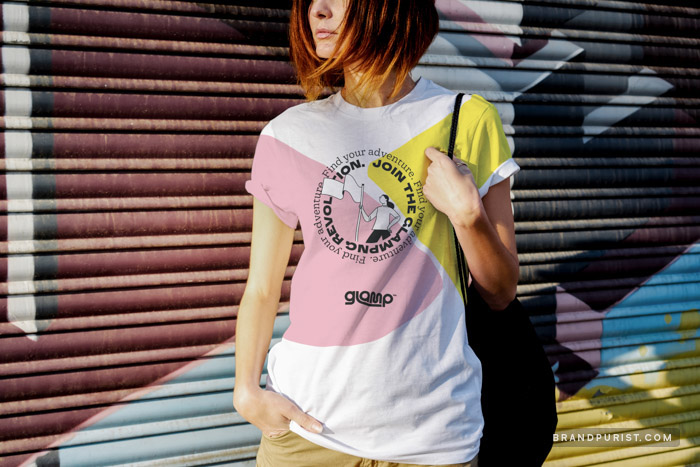 A young woman standing in front of graffiti and wearing a Glamp branded t-shirt. The t-shirt features the messages ‘Find your own adventure’ and ‘Join the glamping revolution’ in bold letters.
