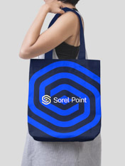 Young woman in front of a grey background carrying a navy tote bag with the Sorel Point logo printed on it.
